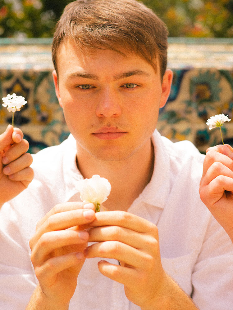 Man in white button-up shirt surrounded by white flowers.