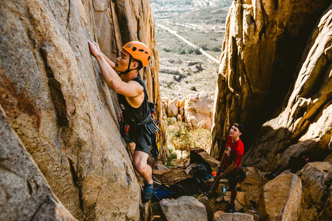 An Asian man rock climbing with belayer in Mission Trails Regional Park.