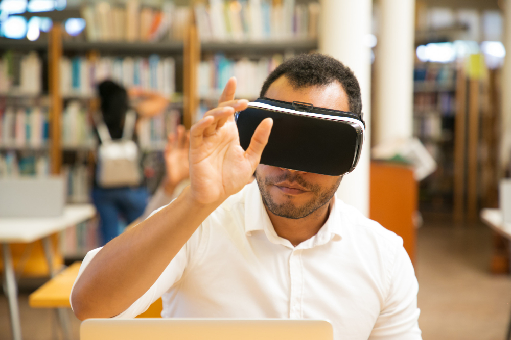 A man in a library wearing a VR headset and lifting his hand mid-air.